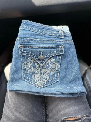 Blå Nine West jeans med broderad ficka - Säljer ett par blå jeans från Nine West med snyggt broderat mönster på bakfickan och dekorativ knapp. Klassisk femficksmodell i mjukt denimtyg. Perfekta för dig som vill ha jeans med lite extra detaljer.