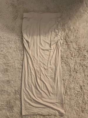Beige långkjol med rynkade detaljer - Lång beige kjol i mjukt och stretchigt material med rynkade detaljer längs ena sidan. Kjolen har en rak och enkel siluett som ger en clean look. Perfekt för dig som gillar stilrena plagg med en twist.
