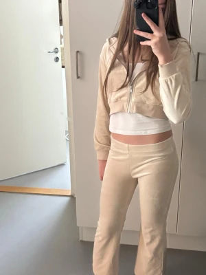 Beige mjukisset från H&M - Säljer ett beige mjukisset från H&M med croppad zip-hoodie och matchande byxor i mjukt velourmaterial. Perfekt för chill dagar hemma. Setet har en enkel och stilren look med dragkedja framtill på hoodien.