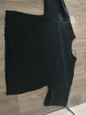 Mörkblå stickad tröja med kort ärm - Mysig mörkblå stickad tröja med korta ärmar och rund hals. Tröjan har en enkel och avslappnad passform med ribbstickade kanter nedtill och vid ärmsluten. Perfekt att matcha med jeans eller kjol för en chill look.