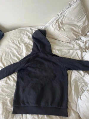 Svart hoodie från Peak Performance - Säljer en svart hoodie från Peak Performance med vit logga på bröstet och klassisk känguruficka. Hoodien har huva med dragsko och ribbade muddar vid ärmslut och nederkant. Perfekt för en chill och stilren look.