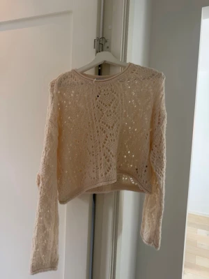 Beige virkad tröja  - Säljer en beige, virkad stickad tröja i storlek M. Tröjan har ett genombrutet mönster, rund halsringning och långa ärmar. Perfekt för lager på lager och ger en bohemisk vibe till din outfit.
