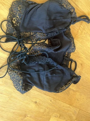 Svart spets linne  - Säljer en svart linne från SHEIN i storlek S. Linnet har tunna axelband, ribbad struktur och vackra spetsdetaljer runt kuporna och kanterna. Materialet är mjukt och lätt, perfekt för dig som gillar en feminin och trendig look.
