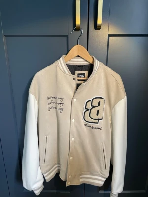 Beige och vit varsityjacka från Zara - Snygg jacka från Zara i oanvänt skick. Köpt i Spanien så tror inte man kan få tag på den i Sverige. Hör av er vid funderingar! 