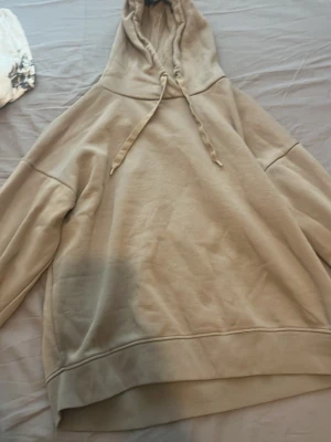 Beige oversized hoodie med huva - Säljer en beige oversized hoodie med huva och dragsko. Hoodien har långa ärmar, ribbade muddar och är gjord i mjukt sweatshirtmaterial. Perfekt för en chill och avslappnad stil.
