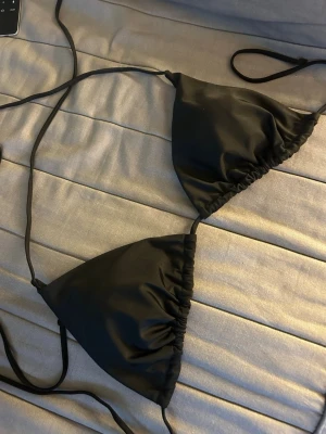 Svart trekantsbikini med knytband - Snygg svart trekantsbikini med tunna knytband som ger en klassisk och stilren look. Perfekt för lata dagar på stranden eller vid poolen. Enkel att justera för bästa passform. Helt oanvänd, storlek 1XL men liten i storlek