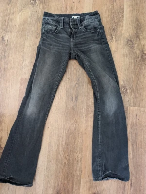 Svarta bootcut jeans med slitningar stl.164 - Säljer ett par svarta bootcut jeans med snygga slitningar och tvättade detaljer på benen. Jeansen har klassisk femficksmodell och normal midja. Perfekta för dig som gillar en avslappnad men trendig look.