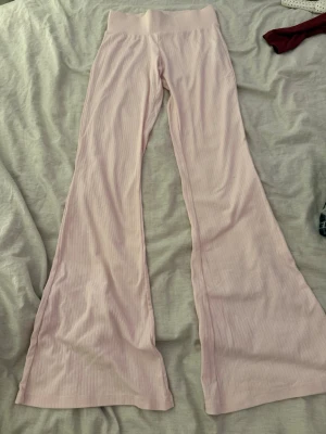 Ljusrosa ribbade utsvängda leggings - Säljer ett par ljusrosa leggings med ribbad struktur och utsvängda ben. Hög midja och mjukt stretchigt material som sitter skönt. Perfekta för en trendig och avslappnad look.