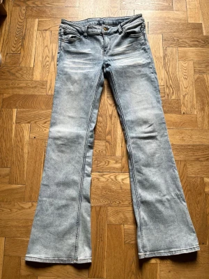 Ljusgrå bootcut Cheap Monday-jeans  - Säljer ett par ljusgrå bootcut jeans med klassisk femficksdesign och utsvängda ben. Jeansen har slitningar och tvättade detaljer framtill för en cool vintagekänsla. Tillverkade i denim med normal midja och knappgylf. Svart-vitt Cheap Monday-märke. 