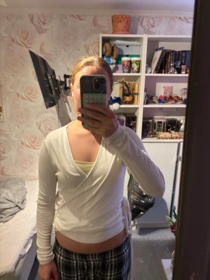 Vit omlottopp med knytband - Säljer en vit långärmad omlottopp med knytband i sidan. Toppen har en djup v-ringning och sitter tajt mot kroppen. Perfekt att styla med höga jeans eller kjol för en trendig look.
