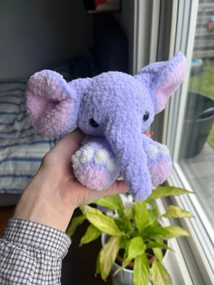 Virkad lila elefant🐘💜 - Supersöt virkad elefant av mitt eget mönster ”Ellie the elephant”! Utan rosetter men är istället gjord med superlurvigt garn! Som syns på bilder kan den både sitta och ligga ner. Denna elefant är ljuslila med vita och ljusrosa detaljer💜🩷 !OBS, innehåller säkerhetsögon som ej rekommenderas för barn under 3 år! 