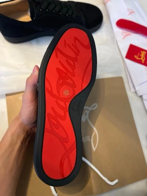 Christian Louboutins svarta - Snygga svarta sneakers från Christian Louboutin med den ikoniska röda sulan och diskret logga undertill. Skorna har svart ovandel i mocka, svarta skosnören och en låg profil som ger en clean och exklusiv look.