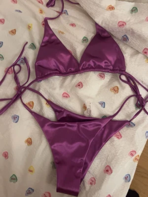 Lila bikini med knyt och trekantsmodell - Säljer en snygg lila bikini i trekantsmodell med knyt både vid sidorna på underdelen och i nacken på överdelen. Materialet har en glansig finish som ger en lyxig känsla. Perfekt för sommaren och strandhäng! Köpte av en tjej på vinted, hon sa hon hade köpt den i Danmark men finns ingen lapp så vet inte var den är ifrån.