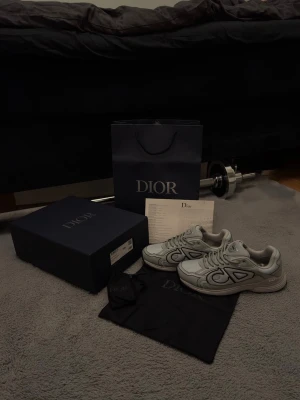 Grå sneakers med CD-detalj - Snygga grå sneakers med stora CD-detaljer på sidorna. Kommer med skobox, extra skosnören, dustbag och en påse. Helt nya ej og! hör gärna av dig innan köp!