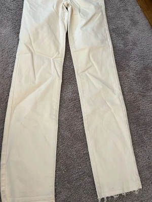 Beiga raka jeans med rå kant - Säljer ett par beiga jeans med rak passform och rå kant längst ner på benen. Jeansen har klassiska bakfickor och är tillverkade i mjuk bomull. Perfekta till en avslappnad och trendig look.