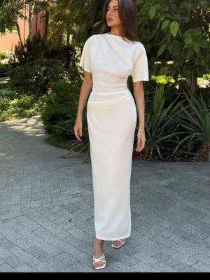 Vit elegant maxiklänning - Snygg vit maxiklänning med korta ärmar och hög hals. Klänningen har en figurnära passform och markerad midja som ger en stilren siluett. Tillverkad i ett mjukt, stretchigt material som sitter bekvämt. Perfekt för dig som vill ha en minimalistisk och chic look.