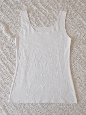 Tezenis vitt sömlöst linne S - Säljer en enkel och stilren vit linnetopp från Tezenis. Toppen är ärmlös med rundad halsringning och har en tight passform. Perfekt att matcha med jeans eller kjol för en clean look.