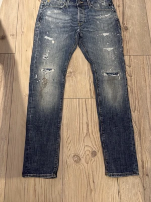 Blå slitna jeans med distressed detaljer - Säljer ett par blå jeans med coola slitningar och feta wash detaljer på både fram- och baksida. Jeansen har en smal passform och klassisk femficksdesign. Perfekta för dig som gillar en avslappnad och trendig stil. Modellen Glenn från Jack And Jones, Hör av er om några frågor och kom gärna med bud!!