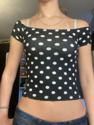 Svart prickig croppad topp - Säljer en svart croppad topp med vita prickar. Toppen har en tight passform och korta ärmar som kan bäras offshoulder. Materialet känns stretchigt och mjukt, från newyorker