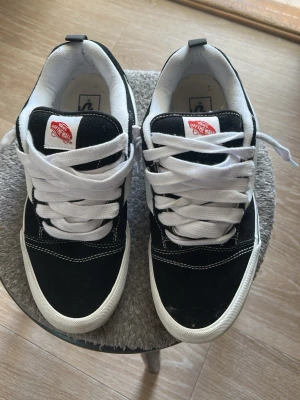 Svartvita Vans Old Skool sneakers - Klassiska Vans Old Skool sneakers i svart och vitt med vit sula och vita skosnören. Skorna har den ikoniska sidostripen och Vans-logga på plösen. Ovandelen är i mocka och canvas, med kontrastsömmar för en snygg look.