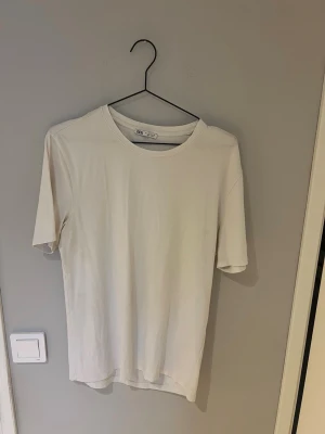 Vit t-shirt från ZARA - En stilren vit t-shirt från ZARA med klassisk rund hals och korta ärmar. Tillverkad i mjuk bomull som känns skön mot huden. Perfekt att matcha med jeans eller shorts för en clean look.