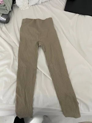Beige ribbade leggings från BikBok - Snygga beige ribbade leggings från BikBok i storlek XS/S. Tillverkade i mjukt material med 90% polyamid och 10% elastan för extra stretch och komfort. Hög midja och smal passform, perfekta till en avslappnad look.