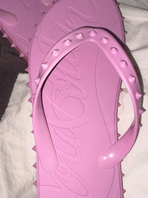 Rosa och röda flip-flops med nitar - Säljer ett par coola flip-flops i plast, en i ljusrosa och en i rött. Remmarna har nitar för en edgy look och sulan har ett mönstrat tryck. Perfekta för sommaren eller stranden!
