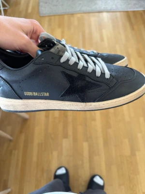 Svarta GGDB Ballstar sneakers - Snygga svarta GGDB Ballstar sneakers i läder med vit sula och grå skosnören. Skorna har en svart stjärna på sidan och guldfärgad text. Klassisk låg modell med perforerade detaljer på tån och retrovibbar.