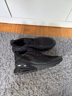 Helvita Nike Air Max 270 sneakers - Säljer ett par helsvarta Nike Air Max 270 sneakers med mesh-ovandel och synlig Air-enhet i hälen. Skorna har en sportig siluett, snörning och diskreta detaljer. Perfekta för dig som gillar stilrena och bekväma sneakers. Använda 2 3 gånger så lite smustiga på undersulan men inget slitet 
