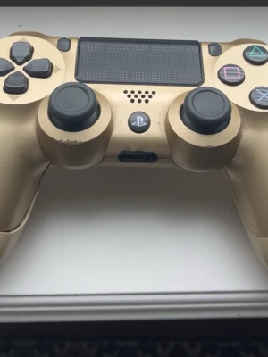 Guldfärgad PS4 DualShock 4 handkontroll - Säljer en guldfärgad PlayStation 4 DualShock 4 handkontroll med touchpad och klassiska PlayStation-knappar. Snygg design med svart detaljering och greppvänlig form, perfekt för gaming.