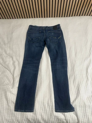 Blå slitna raka jeans  - Säljer ett par blå jeans med raka ben och slitningar på både fram- och baksida. Jeansen har klassisk femficksdesign och en tvättad look med ljusare partier. Perfekta för en avslappnad och trendig stil. Jeansen är ifrån Jack and Jones och är oandvänbara bra för dig som vill ha ett par jeans nu i slutet av sommaren. 