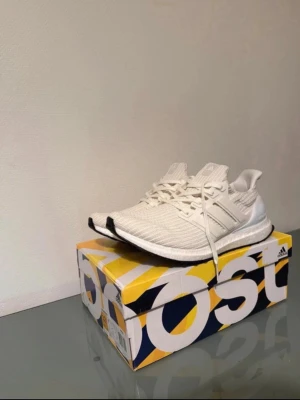 Vita Adidas Ultraboost sneakers - Snygga vita Adidas Ultraboost sneakers med stickad ovandel i mesh och klassiska tre ränder på sidan. Skorna är helt nya och oanvända. Säljer dem för dem inte kommer till användning.