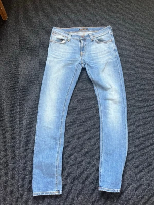 Nudie jeans tight long john - Säljer ett par ljusblå slim fit jeans med klassisk femficksmodell och snygga slitningar framtill. Jeansen har normal midja och raka ben, tillverkade i mjukt denimtyg. Perfekta för en avslappnad och trendig look.