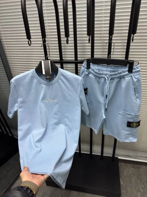 Stone Island Set - Snyggt ljusblått set från Stone Island med t-shirt och shorts. T-shirten har rund hals och diskret logga på bröstet. Shortsen har resår i midjan, dragsko och fickor med Stone Island-märke på benet. Perfekt för en avslappnad och trendig look.