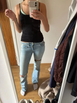 TALL Low waist ljusblå slitna bootcut jeans  - Säljer ett par ljusblå jeans i tall modell med slitningar vid knäna och bakfickan. Jeansen har klassisk femficksmodell, normal midja och är tillverkade i denim. Perfekta för en avslappnad och trendig look.