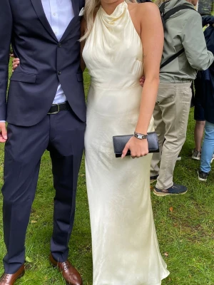Lång vit halterneckklänning i satin - Elegant långklänning i vit satin med halterneck och öppen rygg. Klänningen har en mjukt draperad överdel och slimmad passform som ger en lyxig känsla. Perfekt för speciella tillfällen och studentfirande. Från Meshki 2 år gammal, lite kort då den tvättades efter balen