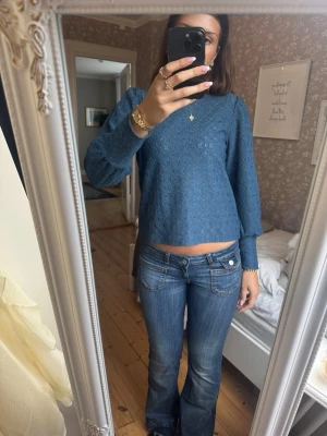 Blå spetsblus med lång ärm - Säljer en blå blus i spets med lång ärm och rak passform. Blusen har ett diskret hålmönster och är något croppad. Perfekt att styla med jeans eller kjol för en trendig look.