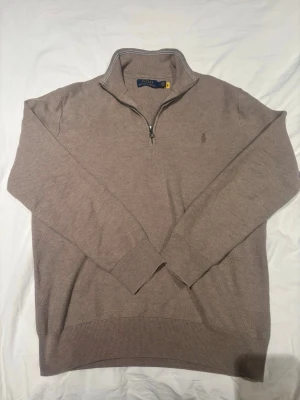 Beige stickad tröja Polo Ralph Lauren - Snygg beige stickad tröja från Polo Ralph Lauren med halv dragkedja den är storlek M men passar xs eftersom den har krympt den är broderad logga på bröstet. Tröjan har ribbade muddar och krage, perfekt för lager på lager. Tillverkad i mjukt material som känns skönt mot huden.