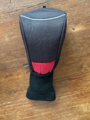 Svart och röd headcover golf - Headcover i svart tyg med röd detalj och diskret mönster på ovansidan. Skyddet har en ribbstickad förlängning för att sitta stadigt på klubban. Perfekt för att skydda driver eller trä klubba.