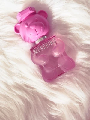 Moschino Toy 2 Bubble Gum parfym - Superfin parfymflaska från Moschino i form av en rosa nallebjörn. Flaskan är gjord av glas och plast, och har ett lekfullt och unikt utseende med tydlig Moschino-logga på bröstet. Perfekt för dig som gillar söta och färgglada detaljer på sminkbordet.