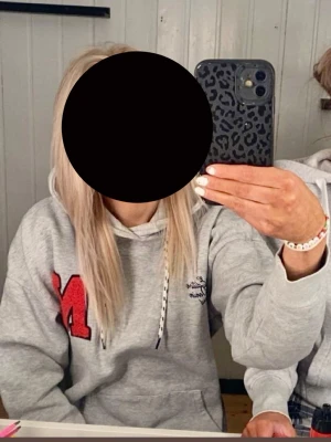Grå hoodie med tryck - Säljer en grå hoodie med stor röd bokstav 'N' på vänster sida. Hoodien har känguruficka framtill och en liten svart textdetalj på bröstet. Perfekt för en avslappnad och trendig look. (Det svart/vita snöret/dragsko i huvan är inte kvar)