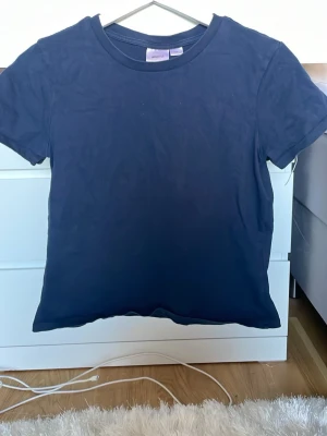 Mörkblå basic t-shirt - En enkel mörkblå t-shirt med rund hals och korta ärmar. T-shirten har en klassisk passform och är tillverkad i mjukt bomullsmaterial. Perfekt att matcha med jeans eller shorts för en clean och stilren look.
