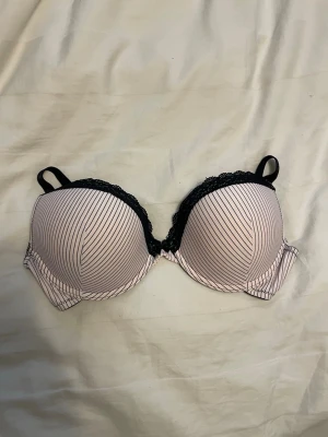 Rosa bh från Victoria’s secret med svarta ränder - Snygg bh från Victoria’s secret gamla modell i ljusrosa med tunna svarta diagonala ränder och svart spetsdetalj längs kuporna. Justerbara axelband och bygel för extra stöd. Perfekt för dig som vill ha en bh med både stil och komfort. Lapp ej kvar dock. 