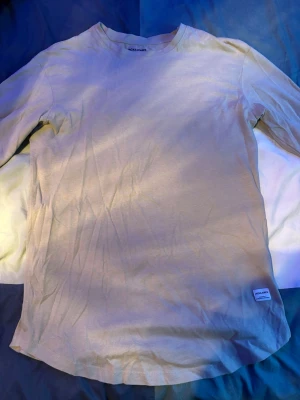 Beige långärmad t-shirt Jack & Jones - En stilren beige långärmad t-shirt från Jack & Jones. Klassisk rund halsringning och diskret logolapp nertill. Tillverkad i mjuk bomull som känns skön mot huden. Perfekt för en enkel och clean look.