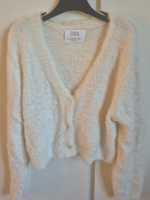 Fluffig vit kofta från ZARA - Supermjuk och fluffig vit kofta från ZARA med v-ringning och knäppning framtill. Koftan har lång ärm och en croppad passform. 