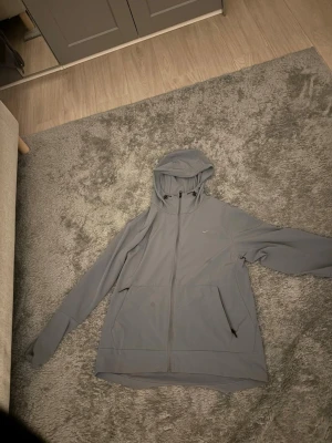 En grå Nike tun jacka  - Snygg grå tun jacka från Nike med hel dragkedja framtill Hoodien har en klassisk huva och diskret Nike-logga på bröstet. Tillverkad i ett mjukt och bekvämt material som passar perfekt till en avslappnad stil. Funkar att använda när man gymmar och joggar         Helt ny säljer för inte vill ha den fick en annan grå jacka 