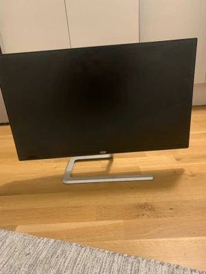 AOC tunn datorskärm svart - Snygg och modern datorskärm från AOC med tunn ram och stilren silverfärgad fot. Skärmen är svart och har HDMI- och VGA-portar på baksidan. Perfekt för gaming, studier eller filmkvällar. Passar bra på skrivbordet tack vare sin minimalistiska design.