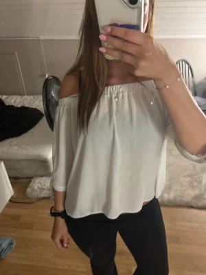 Vit offshoulder blus med knyt - Säljer en söt vit offshoulder blus med trekvartsärm och knytband vid ärmsluten. Blusen har en luftig passform och är perfekt för varma dagar. Enkel att styla med både jeans och kjol.