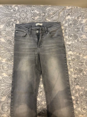 Gråa utsvängda jeans - Säljer ett par gråa jeans med utsvängda ben och klassisk femficksdesign. Jeansen har en ljus tvätt och raka, vida ben som ger en retrovibe. Perfekta för dig som vill ha en avslappnad men ändå trendig look.