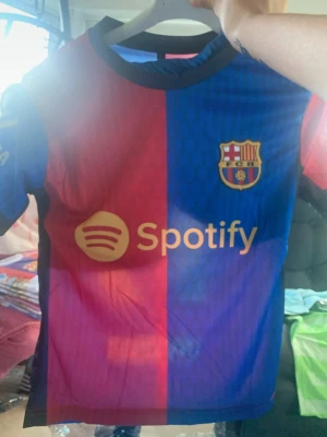 Barcelona matchtröja Lamine Yamal - Säljer en FC Barcelona matchtröja i rött och blått med Spotify-logga på framsidan och Lamine Yamal samt nummer 19 på ryggen. Tröjan har klubbmärket på bröstet och är tillverkad i ett lätt, andningsbart material. Perfekt för fotbollsträning eller att bära till vardags.